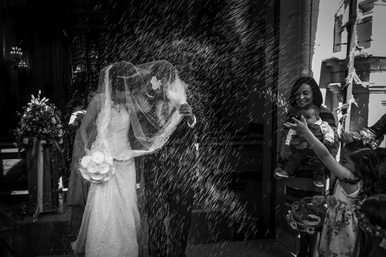 Beautiful monochrome capture of a newlywed couple showered with rice outside a church.
